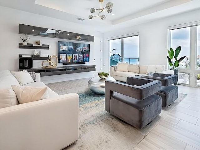 living room with a raised ceiling, a wealth of natural light, and a chandelier