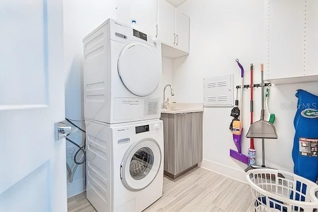 clothes washing area with cabinets, light hardwood / wood-style floors, stacked washer / dryer, and sink