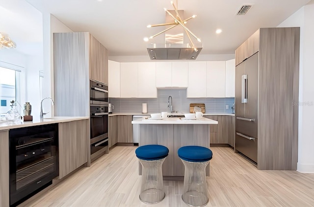 kitchen with white cabinetry, beverage cooler, light hardwood / wood-style flooring, decorative light fixtures, and a center island with sink