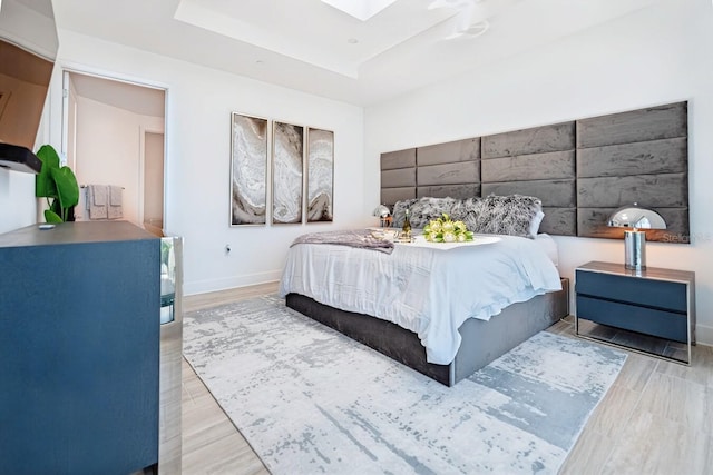 bedroom featuring a raised ceiling, light wood-type flooring, and a skylight