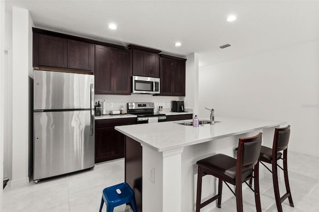 kitchen featuring a center island with sink, appliances with stainless steel finishes, light tile patterned floors, sink, and a kitchen breakfast bar