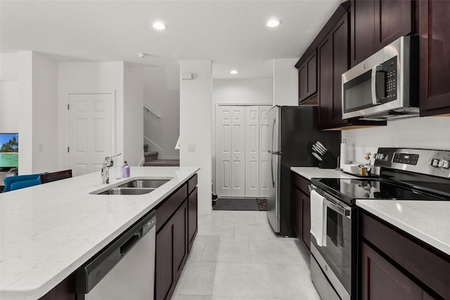 kitchen with stainless steel appliances, a center island with sink, sink, light tile patterned flooring, and light stone countertops