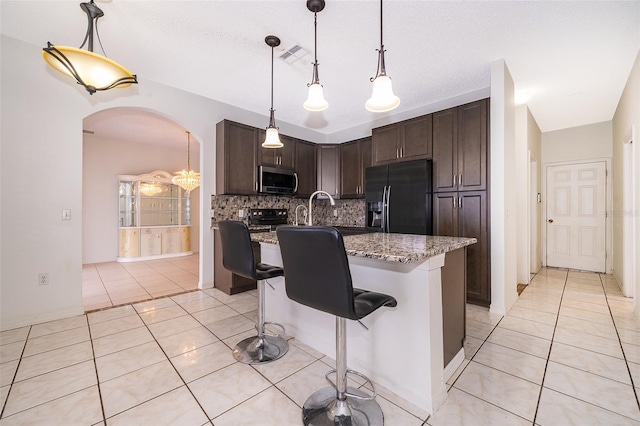 kitchen with black appliances, a breakfast bar area, hanging light fixtures, light stone countertops, and dark brown cabinets