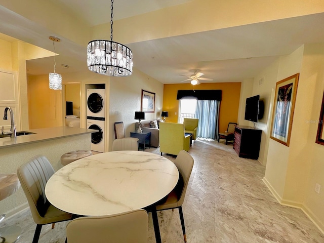 dining area with ceiling fan with notable chandelier, sink, and stacked washer / dryer