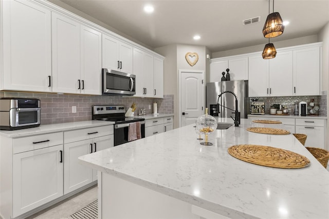 kitchen with light stone countertops, hanging light fixtures, backsplash, white cabinets, and appliances with stainless steel finishes