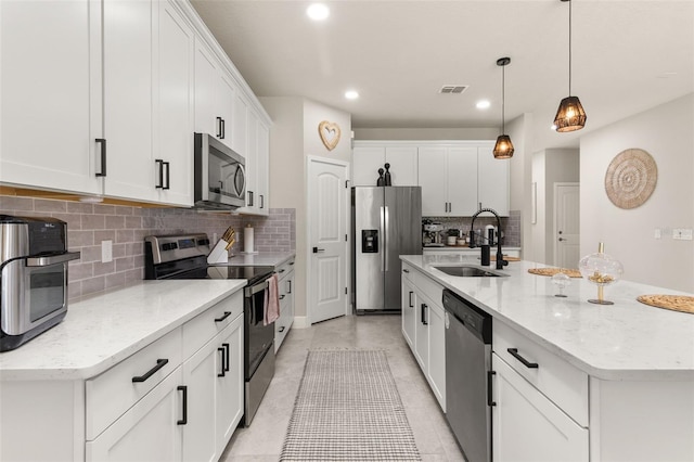 kitchen with white cabinets, stainless steel appliances, hanging light fixtures, and an island with sink