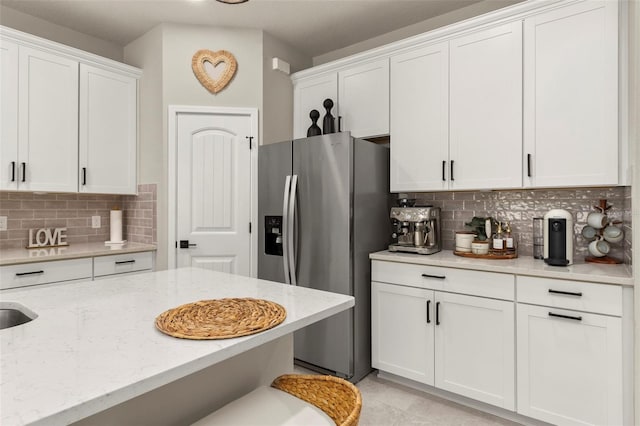 kitchen featuring white cabinets, stainless steel fridge with ice dispenser, tasteful backsplash, and light stone counters