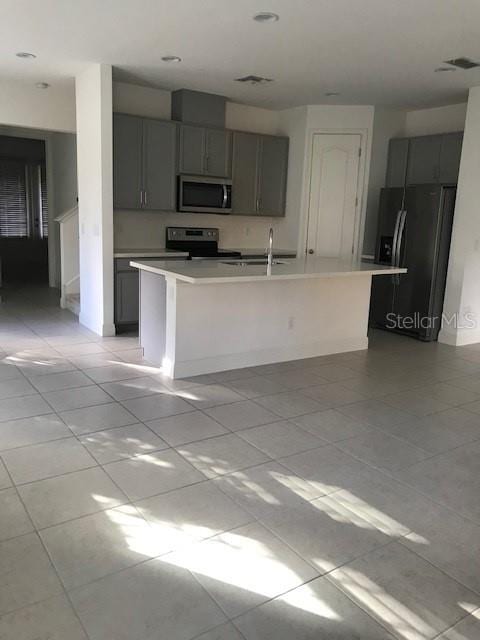 kitchen featuring gray cabinetry, an island with sink, light tile patterned flooring, and stainless steel appliances