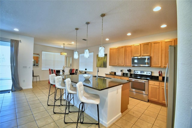 kitchen featuring appliances with stainless steel finishes, pendant lighting, sink, an island with sink, and a breakfast bar