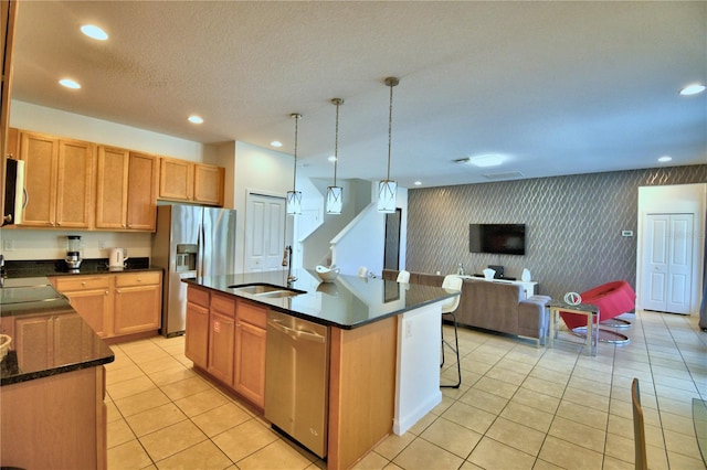 kitchen featuring light tile patterned flooring, a center island with sink, appliances with stainless steel finishes, decorative light fixtures, and sink