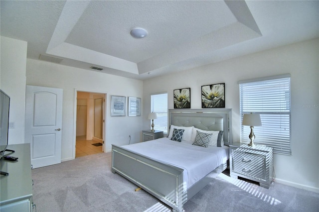 carpeted bedroom featuring a tray ceiling, a textured ceiling, and ensuite bathroom