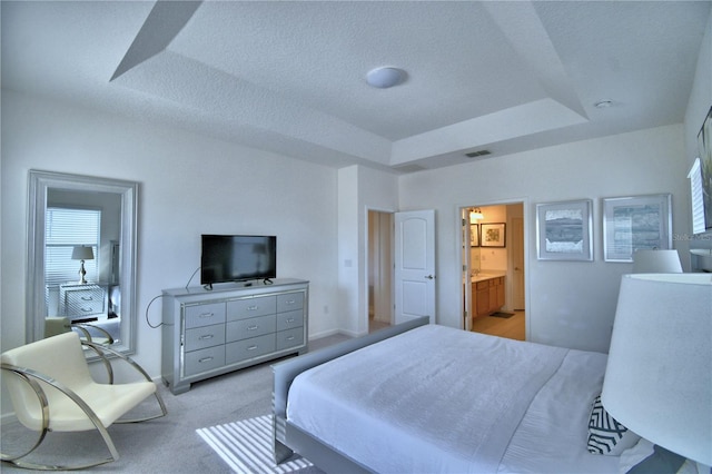 carpeted bedroom with a textured ceiling, a raised ceiling, and ensuite bathroom