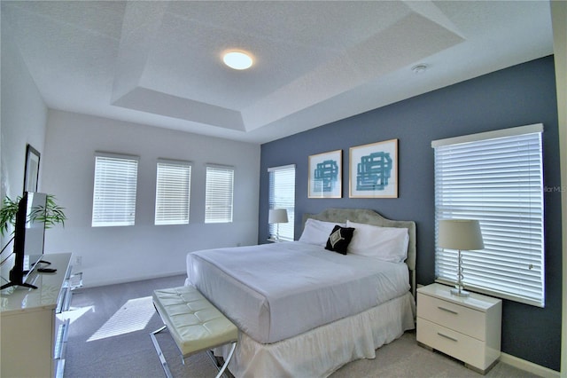 bedroom with a textured ceiling, light carpet, and a tray ceiling