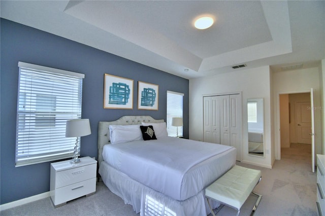 bedroom with light colored carpet, a raised ceiling, and a closet