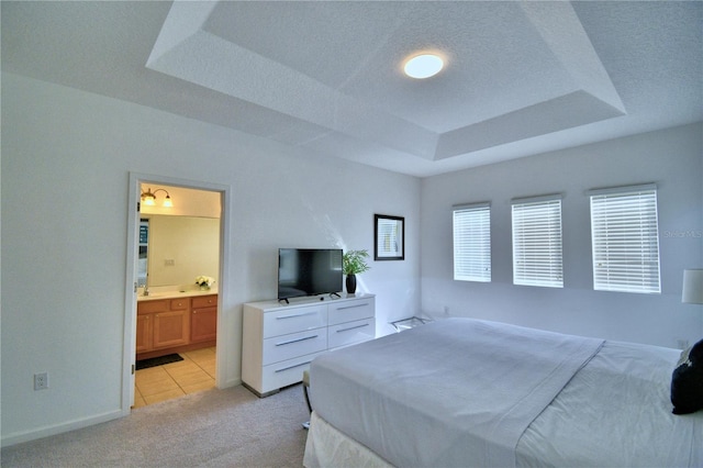 carpeted bedroom with a textured ceiling, a tray ceiling, and connected bathroom