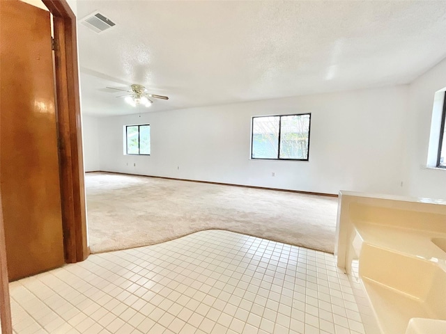 carpeted empty room with ceiling fan, a healthy amount of sunlight, and a textured ceiling