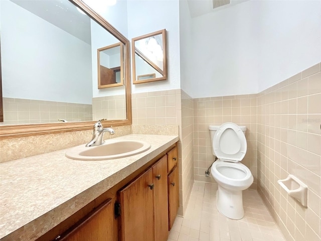 bathroom with tile walls, toilet, vanity, and tile patterned floors