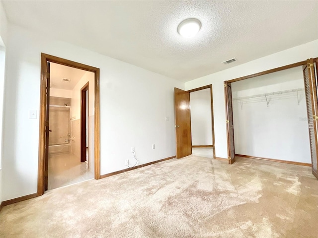 unfurnished bedroom with a textured ceiling, ensuite bath, light carpet, and a closet