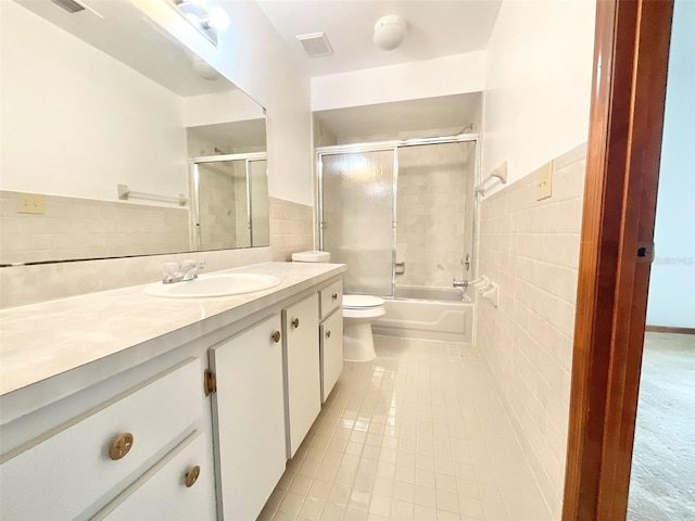 full bathroom with shower / bath combination with glass door, vanity, tile patterned floors, toilet, and tile walls