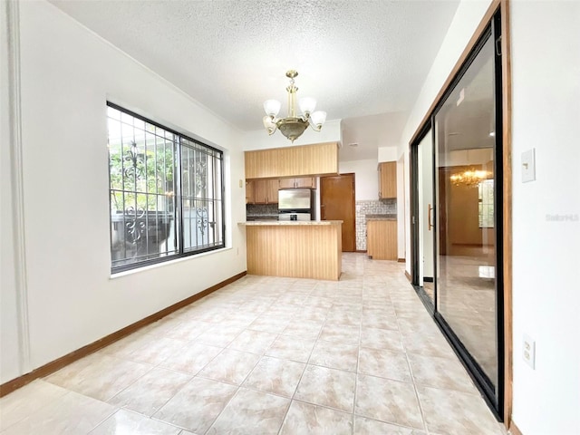 kitchen with kitchen peninsula, a textured ceiling, an inviting chandelier, stainless steel fridge, and decorative backsplash