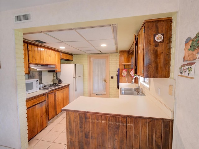 kitchen featuring light tile patterned flooring, a paneled ceiling, white appliances, sink, and kitchen peninsula