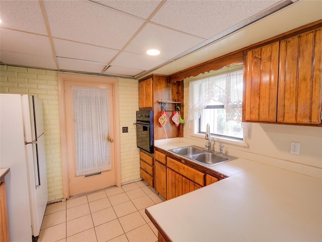 kitchen featuring black oven, a paneled ceiling, sink, and white refrigerator