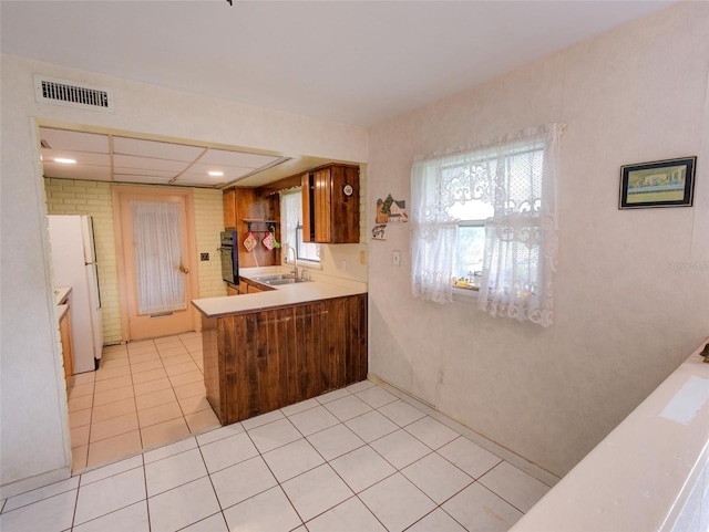 kitchen featuring black oven, white refrigerator, light tile patterned floors, sink, and kitchen peninsula