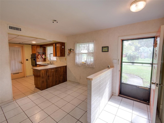 kitchen featuring black oven, kitchen peninsula, light tile patterned floors, and plenty of natural light