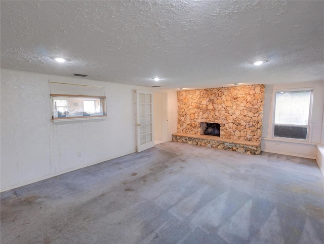 unfurnished living room with a fireplace, a healthy amount of sunlight, a textured ceiling, and carpet