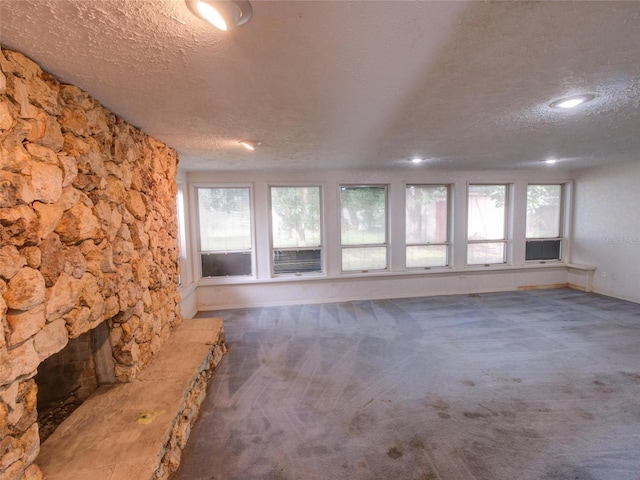 unfurnished living room featuring a stone fireplace, carpet floors, and a textured ceiling