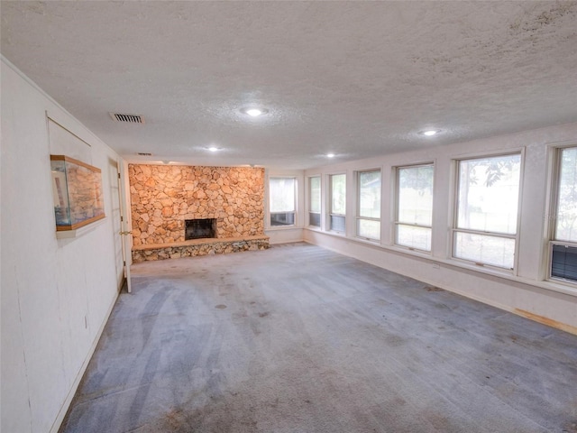 unfurnished living room with a stone fireplace, a wealth of natural light, a textured ceiling, and carpet flooring