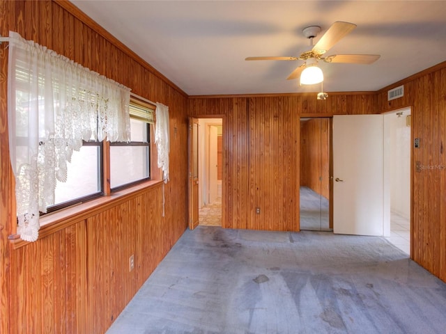 carpeted spare room with ceiling fan, wooden walls, and crown molding