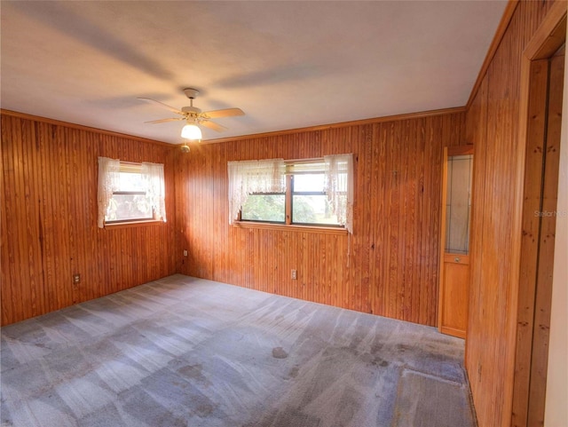 carpeted empty room featuring ornamental molding, wooden walls, and ceiling fan