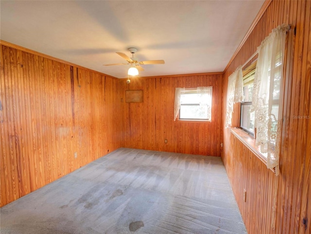 carpeted spare room featuring wooden walls, ceiling fan, and crown molding