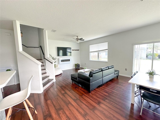 living room with a textured ceiling, ceiling fan, and dark wood-type flooring