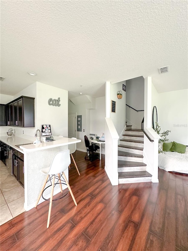 kitchen featuring dark brown cabinets, a textured ceiling, dark hardwood / wood-style floors, and a breakfast bar area