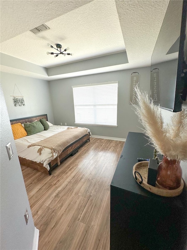 bedroom featuring hardwood / wood-style flooring, a raised ceiling, and a textured ceiling