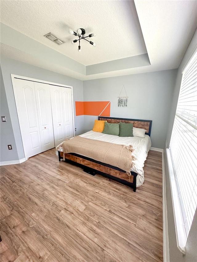 bedroom featuring a tray ceiling, a closet, light hardwood / wood-style flooring, and a textured ceiling