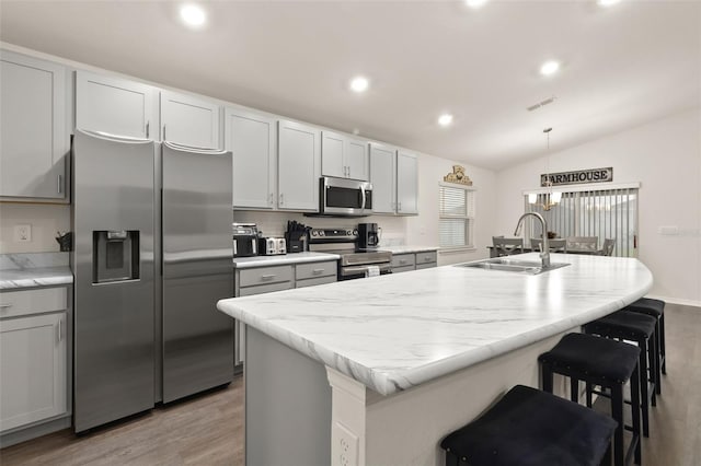 kitchen with light hardwood / wood-style floors, appliances with stainless steel finishes, lofted ceiling, and a center island with sink