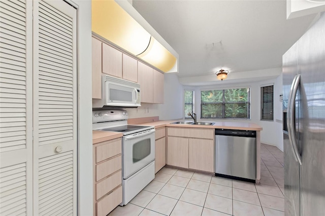 kitchen with kitchen peninsula, sink, light tile patterned floors, light brown cabinets, and appliances with stainless steel finishes