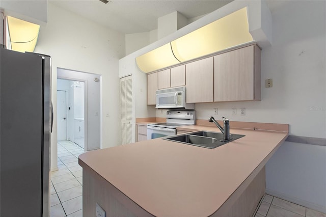 kitchen with light tile patterned floors, white appliances, sink, and kitchen peninsula