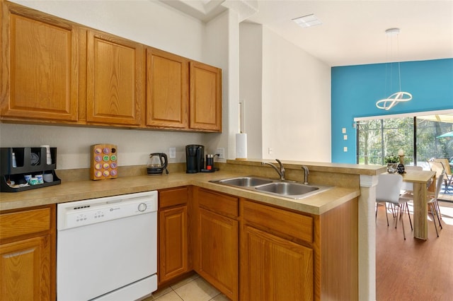 kitchen with dishwasher, kitchen peninsula, hanging light fixtures, sink, and light hardwood / wood-style flooring