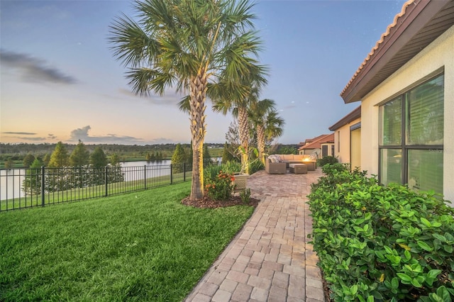 yard at dusk with outdoor lounge area, a water view, and a patio area