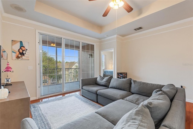 living room featuring hardwood / wood-style flooring, ceiling fan, a raised ceiling, and crown molding