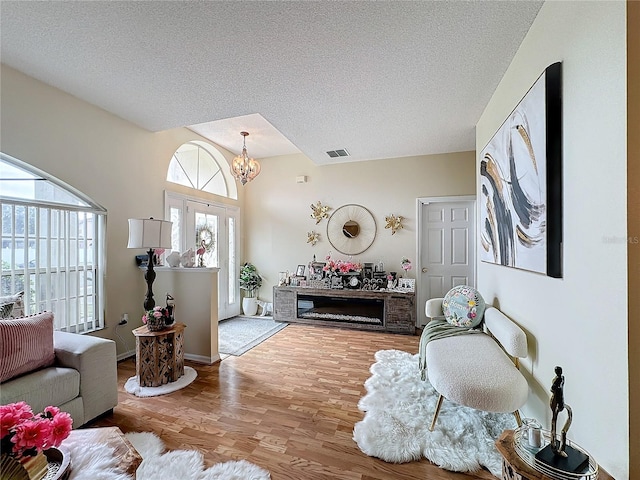 living room with light wood-type flooring, a wealth of natural light, a textured ceiling, and an inviting chandelier