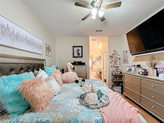 bedroom with connected bathroom, light wood-type flooring, a textured ceiling, and ceiling fan