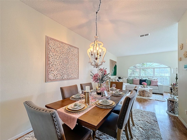 dining room featuring hardwood / wood-style floors, a textured ceiling, lofted ceiling, and a notable chandelier