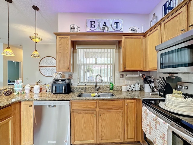 kitchen with sink, appliances with stainless steel finishes, light stone countertops, pendant lighting, and decorative backsplash