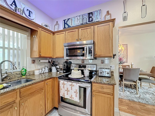 kitchen featuring dark stone counters, sink, tasteful backsplash, light wood-type flooring, and appliances with stainless steel finishes