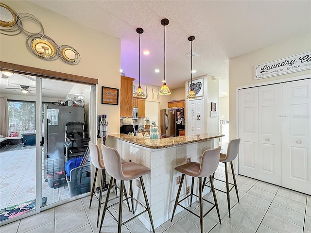 kitchen with a kitchen bar, stainless steel appliances, kitchen peninsula, ceiling fan, and stone countertops